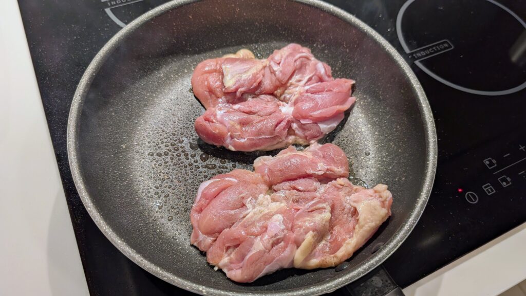 Raw halal chicken thighs coated in potato starch, cooking in a frying pan